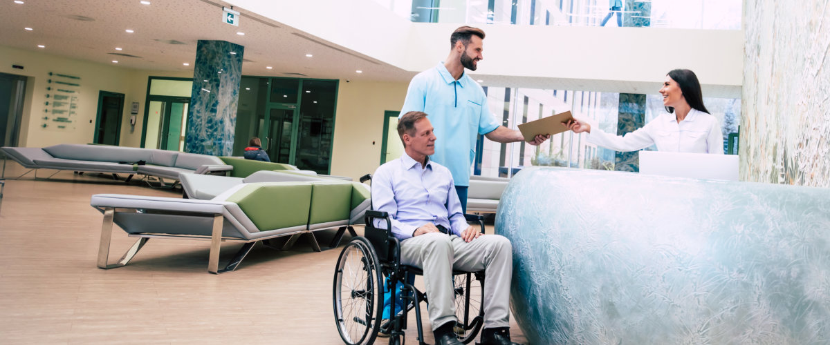 man in a wheelchair is moving in the hospital with help of medical special staff